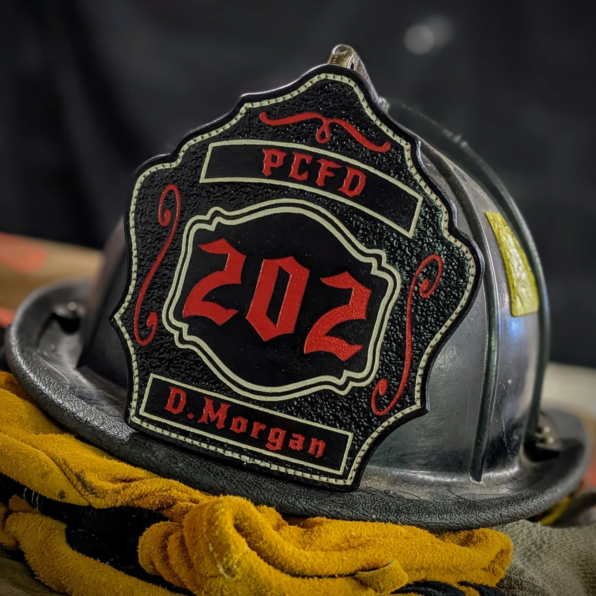 Custom black leather firefighter helmet shield with number 202 in red, red banners, and scroll accents