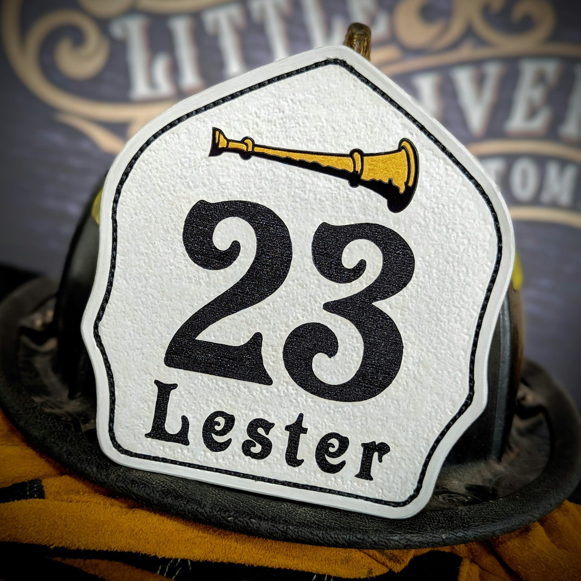 White leather firefighter helmet shield with bold black numbers, gold bugle detail, and custom department lettering.