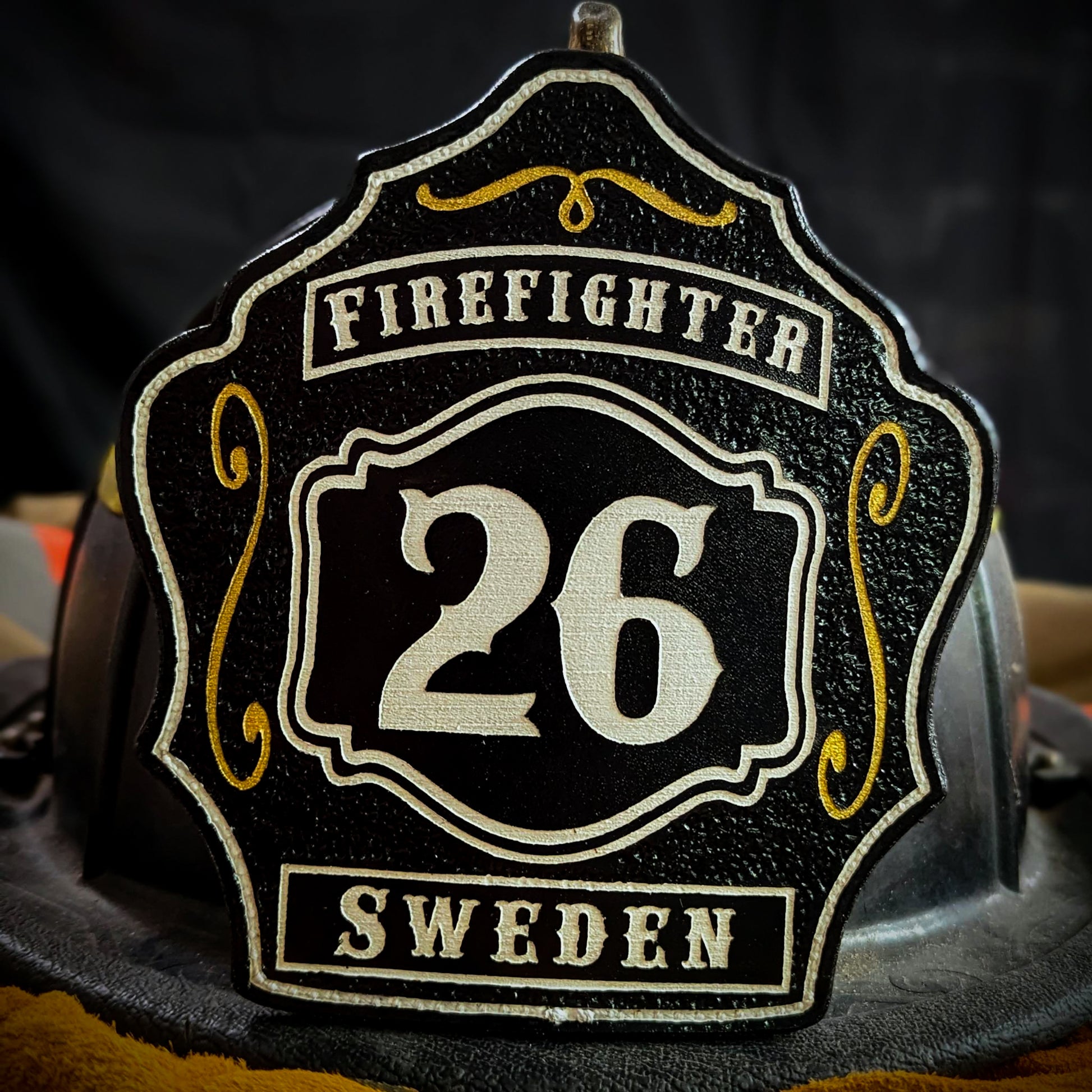 Custom black leather firefighter helmet shield with number 26 in white, gold scroll accents, and bold firefighter text