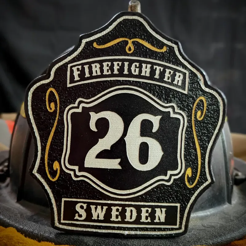 Custom black leather firefighter helmet shield featuring white number 26, firefighter banner across the top, and Sweden nameplate at the bottom with gold accent scrollwork.