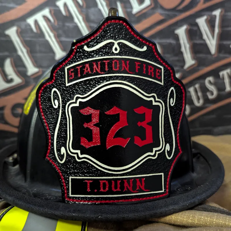 Custom black leather firefighter helmet shield with red number 323, Stanton Fire banner at the top, T. Dunn nameplate at the bottom, and white decorative trim accents.