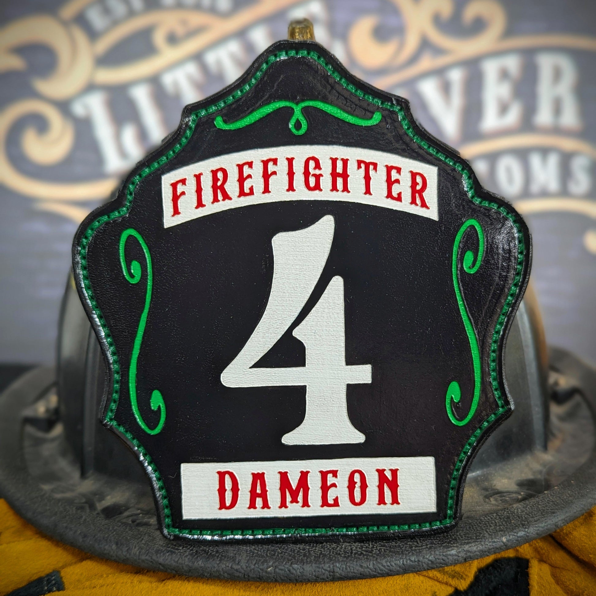 Black leather firefighter helmet shield with white number 4, red Firefighter text above, and name Dameon at the bottom with green detailing.
