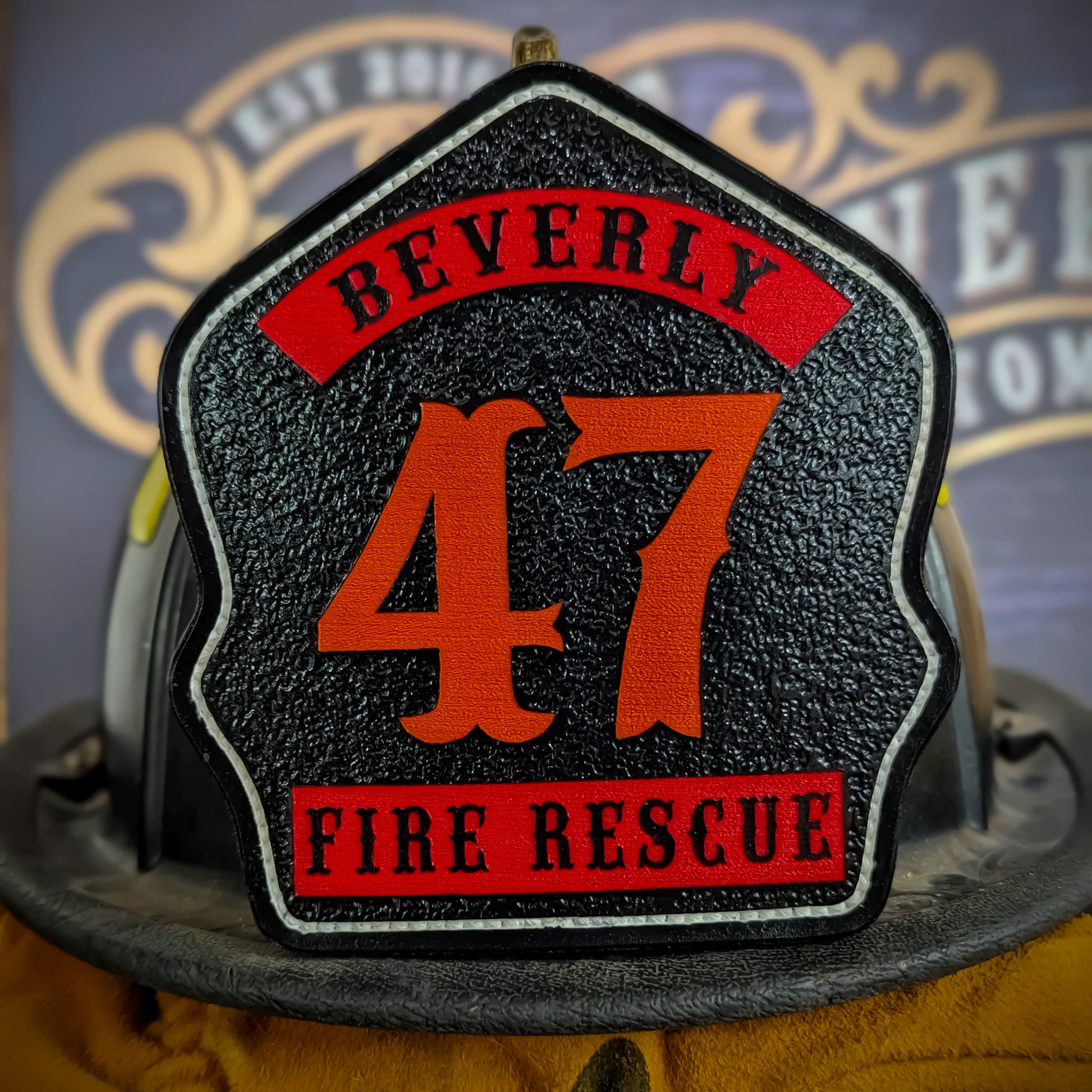 Black leather firefighter helmet shield with bold orange number 47, red panels reading Beverly and Fire Rescue, white border trim, mounted on a fire helmet.