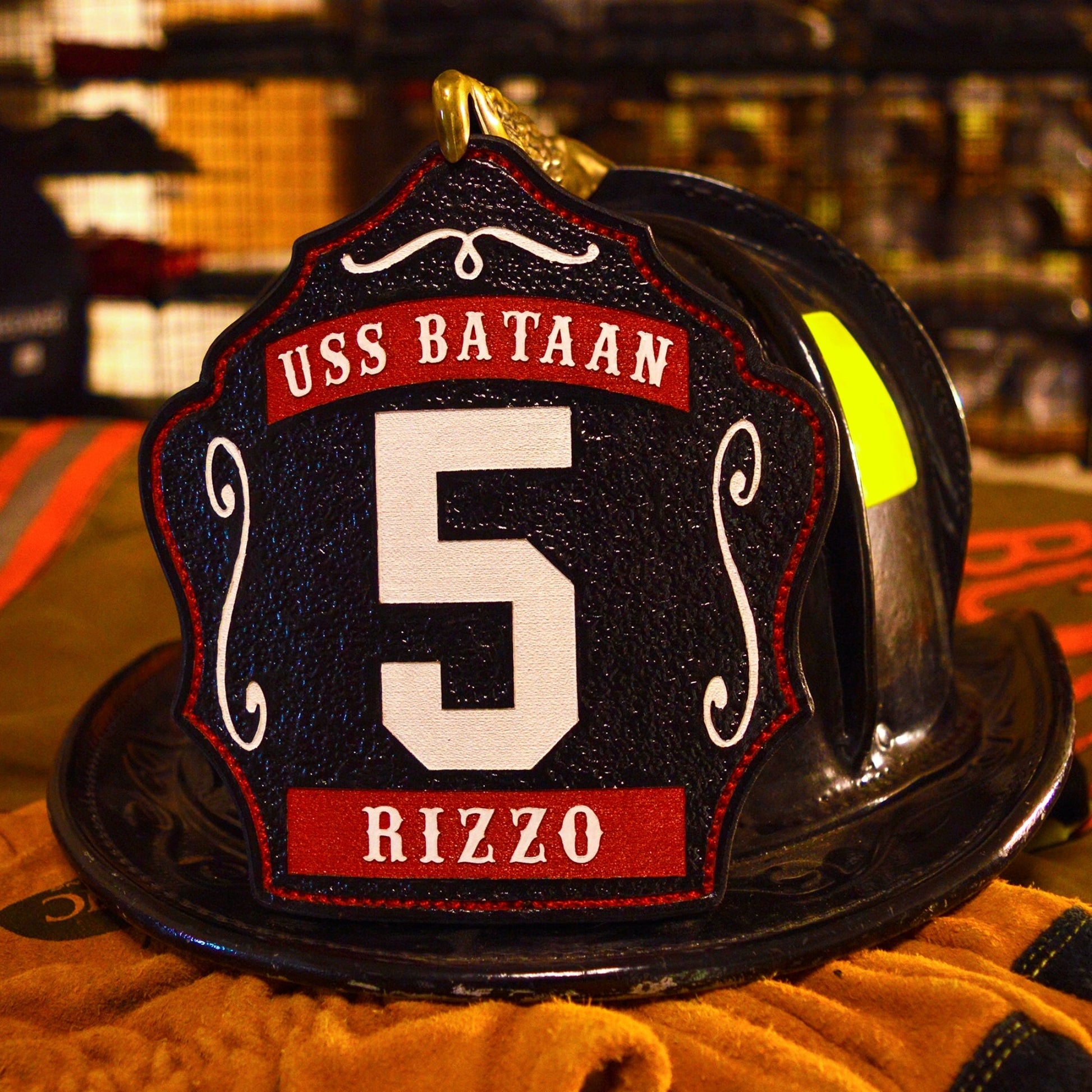 Black leather firefighter helmet shield with bold white number 5, USS Bataan text above, and name Rizzo at the bottom in red panels.