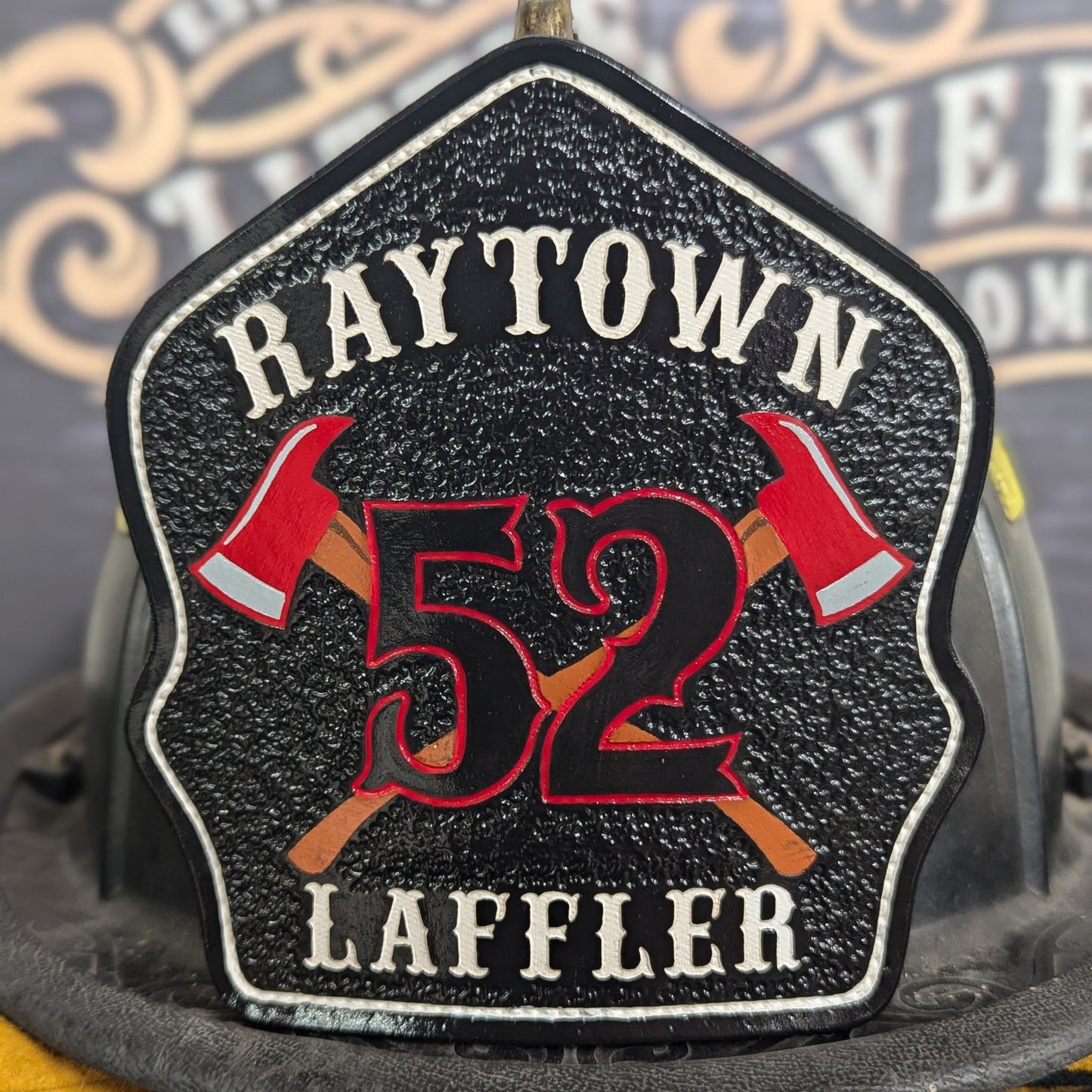 Black leather firefighter helmet shield with crossed red axes and bold red number 52, custom fire department gear.
