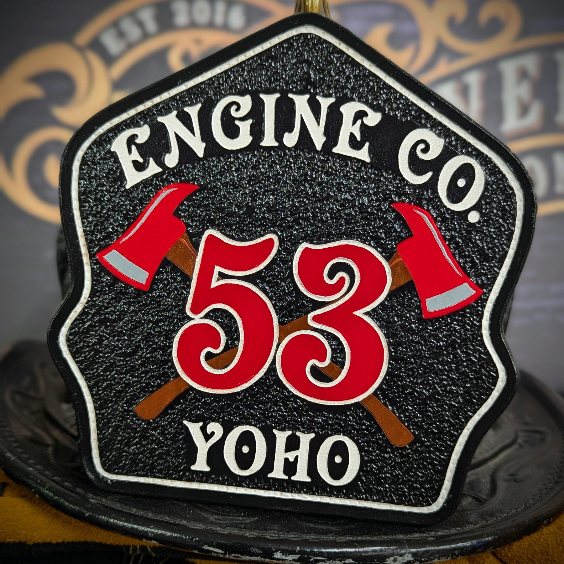 Black leather firefighter helmet shield with crossed red axes and bold red number 53, custom fire department gear.