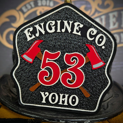 Black leather firefighter helmet shield with crossed red axes and bold red number 53, custom fire department gear.