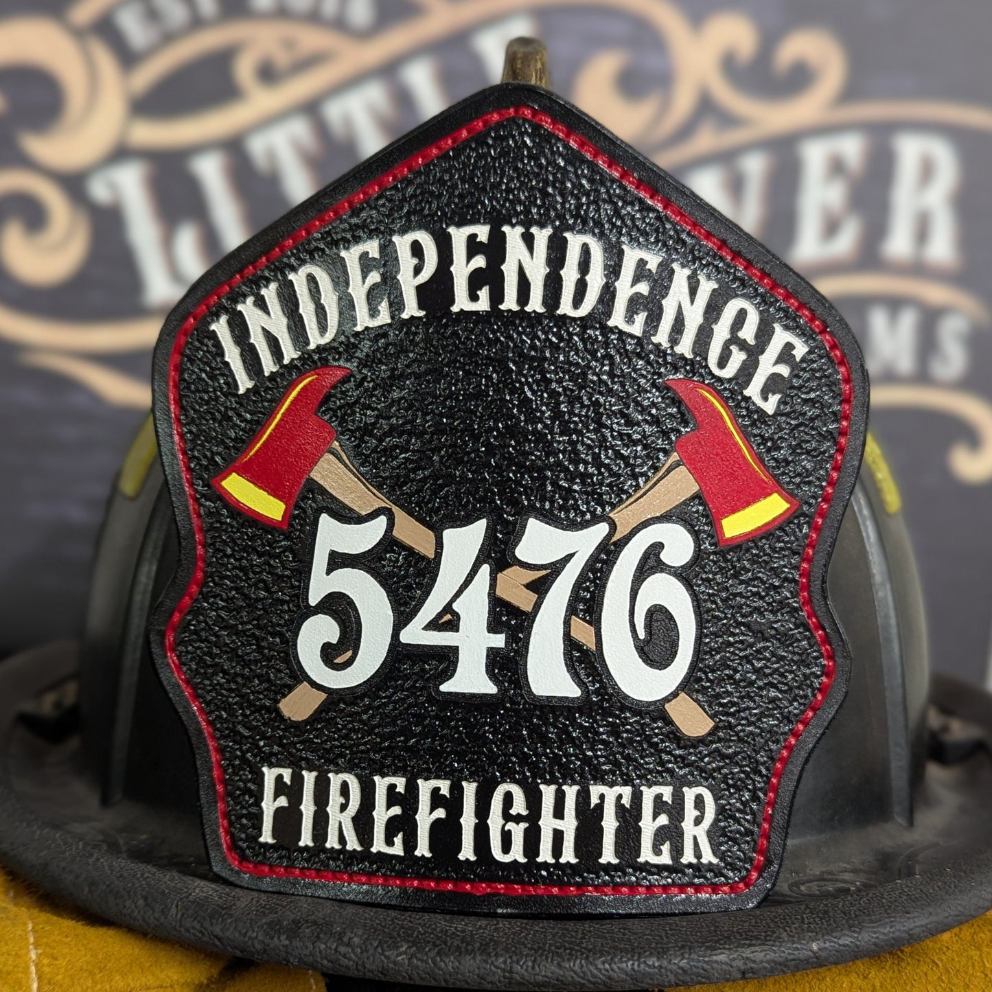 Black leather firefighter helmet shield with crossed red axes and bold white number 5476, custom fire department gear.
