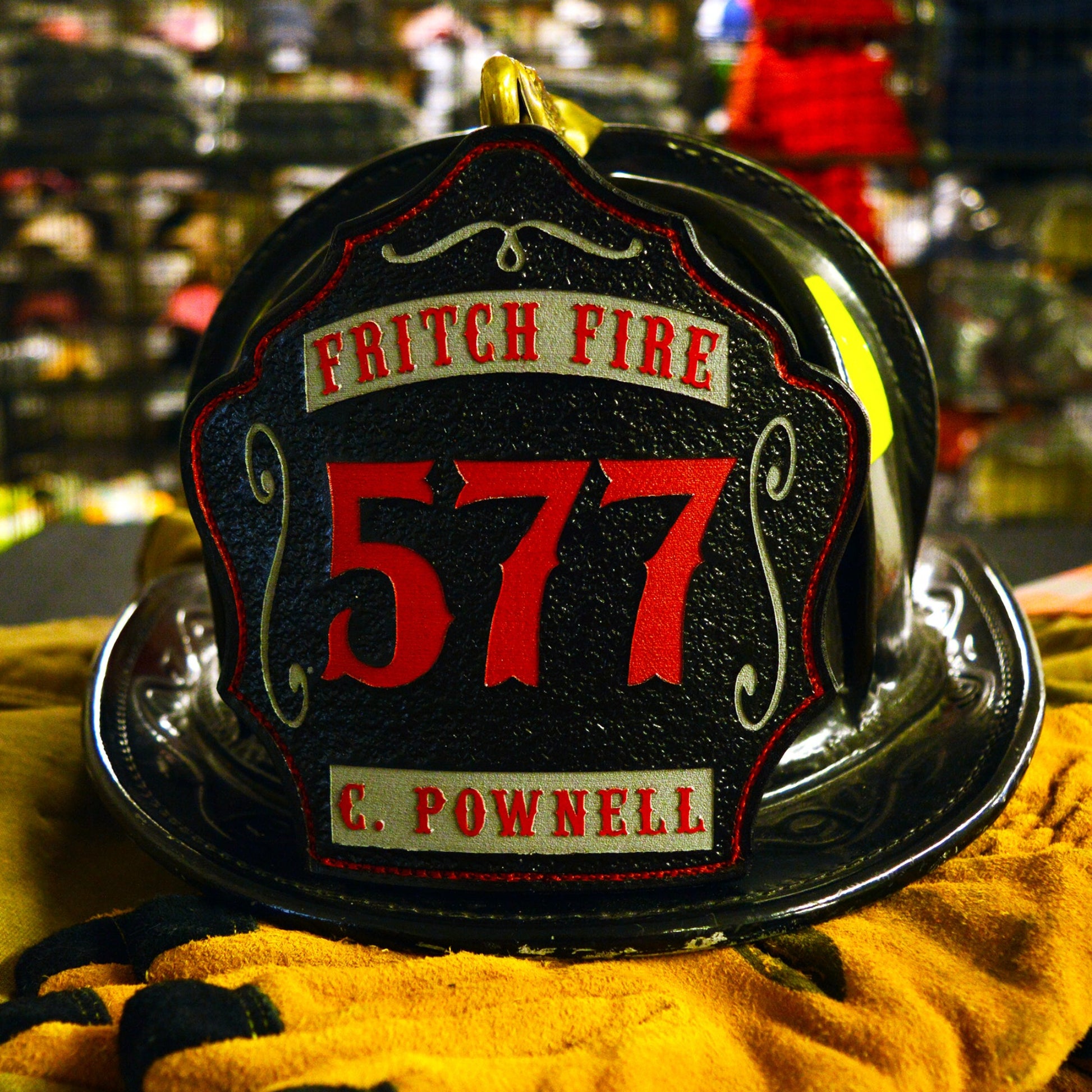Black leather firefighter helmet shield with bold red number 577, silver top banner reading Fritch Fire, and bottom banner C. Pownell in silver with red border detailing.