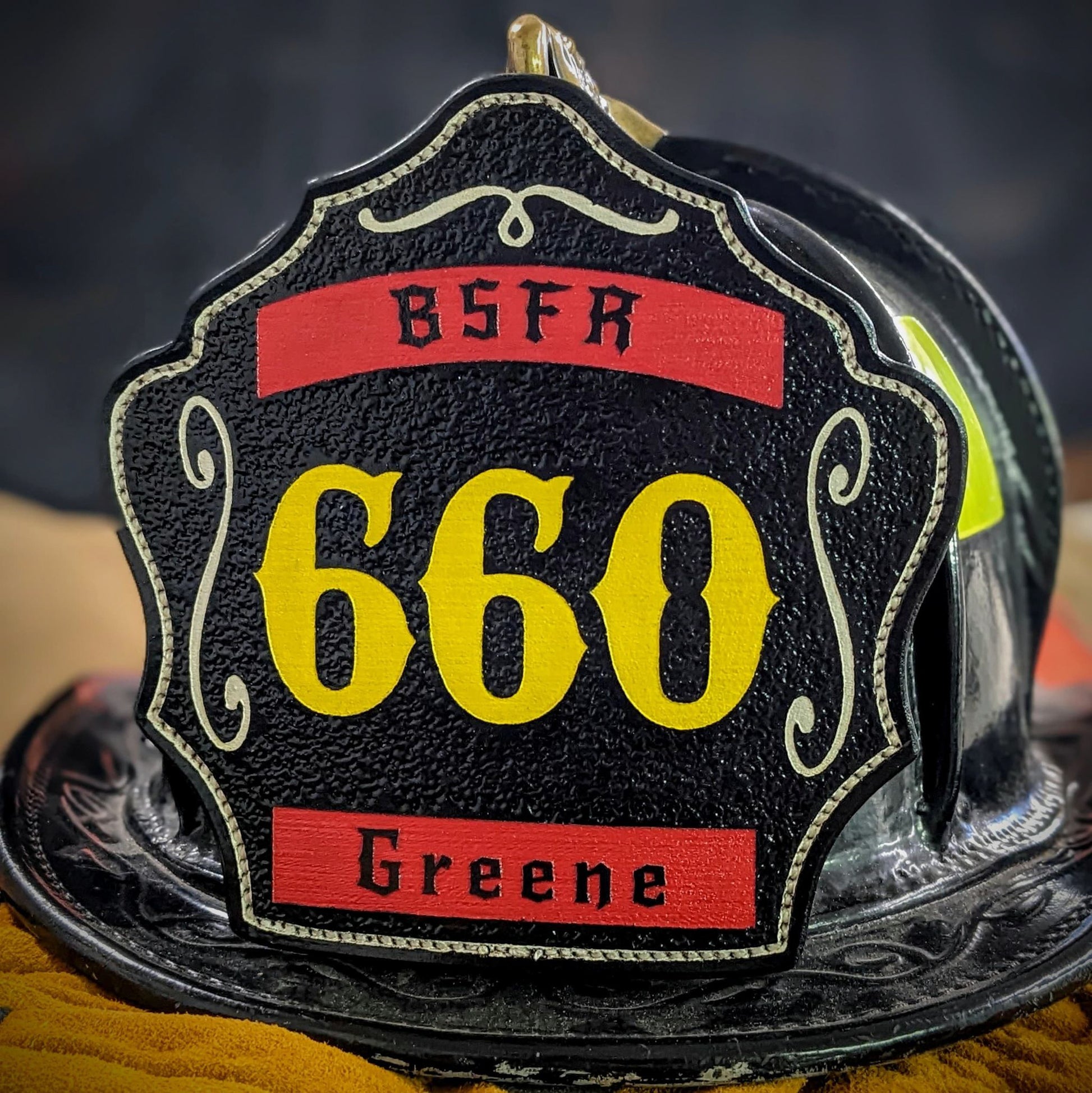 Custom black leather firefighter helmet shield with number 660 in yellow, red name banners, and BSFR lettering