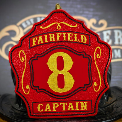 Red leather firefighter helmet shield with bold gold number 8, Fairfield text above, and Captain title at the bottom.