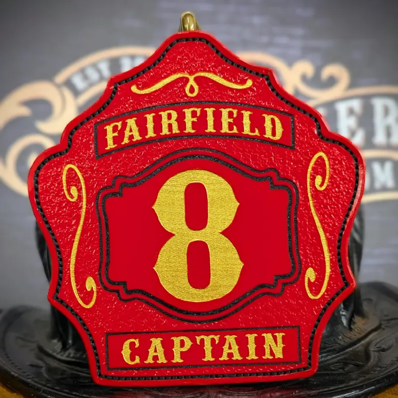 Custom red leather firefighter helmet shield with bold gold number 8, Fairfield banner across the top, Captain title at the bottom, and black outline detailing.