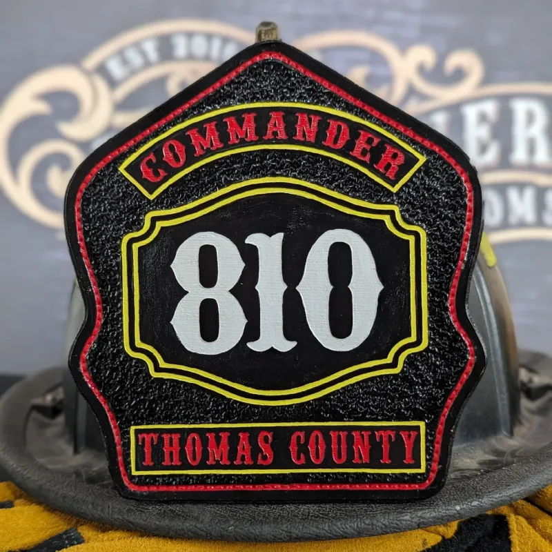 Custom firefighter helmet shield with Commander rank, number 810, and Thomas County lettering in black, red, and yellow leather design.