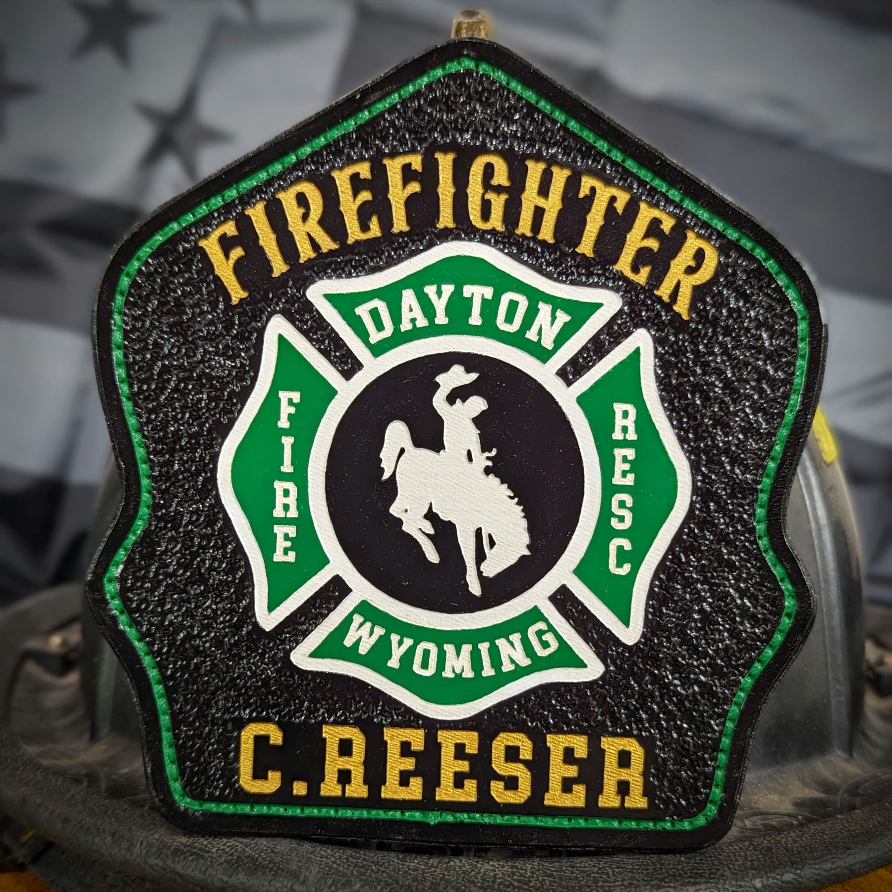 Black leather firefighter helmet shield with green Maltese cross and bucking horse emblem