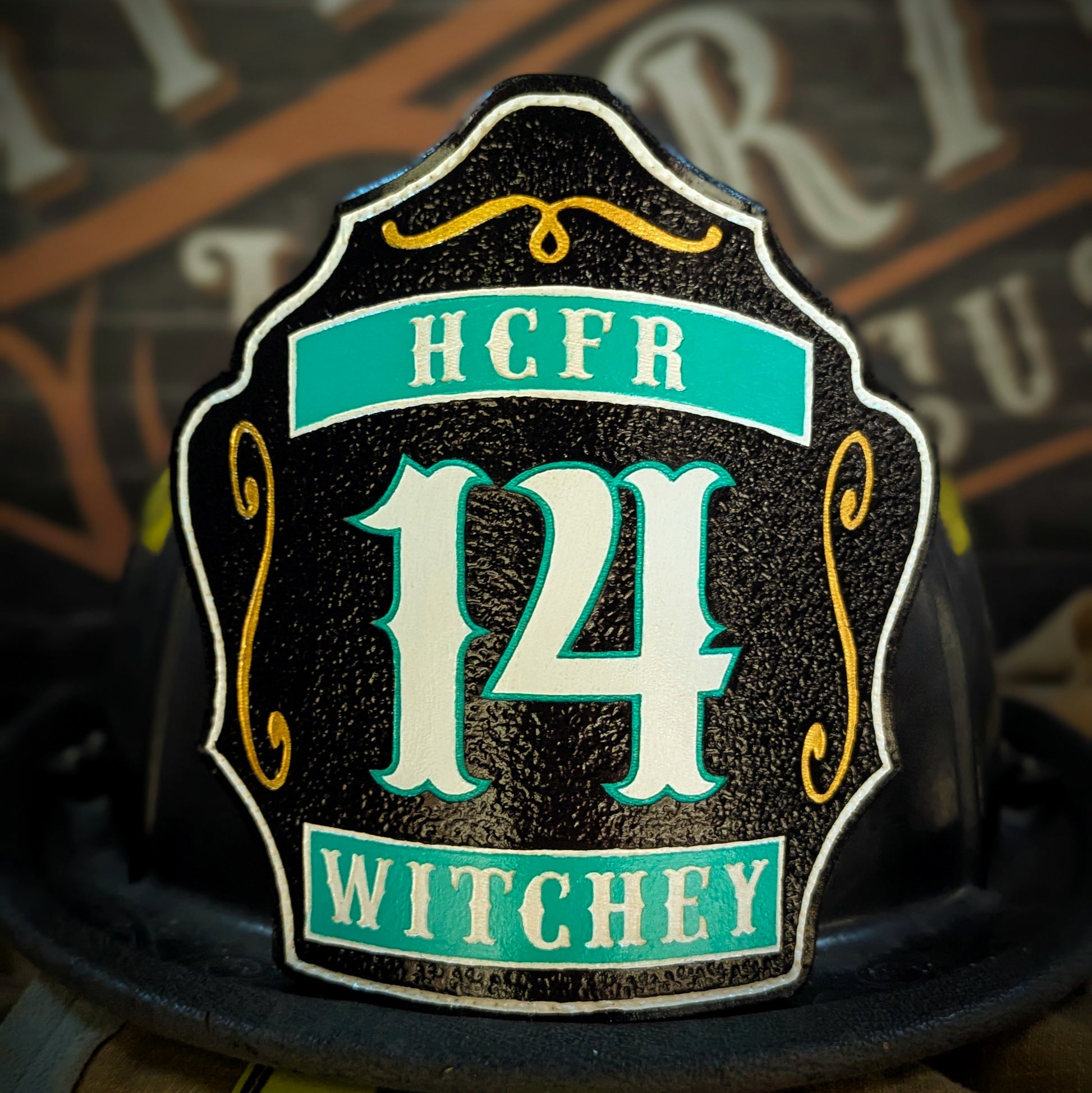 Black leather firefighter helmet shield with teal HCFR and Witchey text, large white 14 number, and gold scroll details.