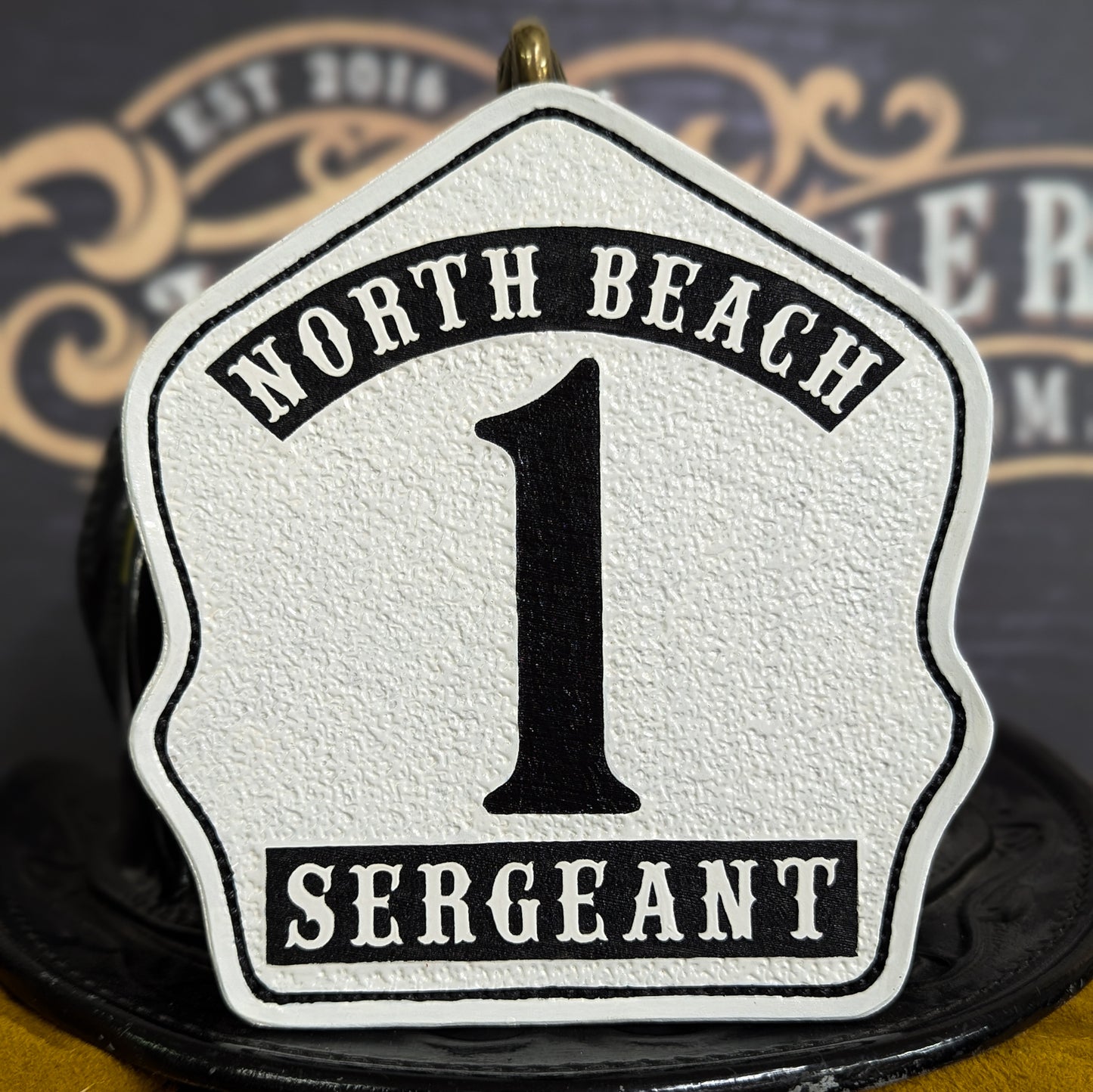 White leather firefighter helmet shield with black number 1, North Beach lettering, and Sergeant rank in bold.