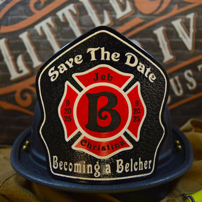 Custom firefighter helmet shield with a black background, red Maltese cross, bold letter B, and personalized wedding details for Jeb and Christina with "Save The Date" and "Becoming a Belcher" text.