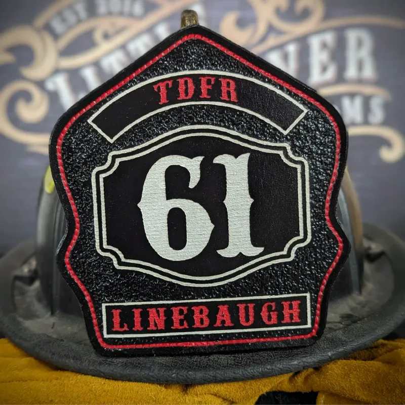 Custom leather firefighter helmet shield with TDFR text, large number 61, and Linebaugh name in black, red, and white design.