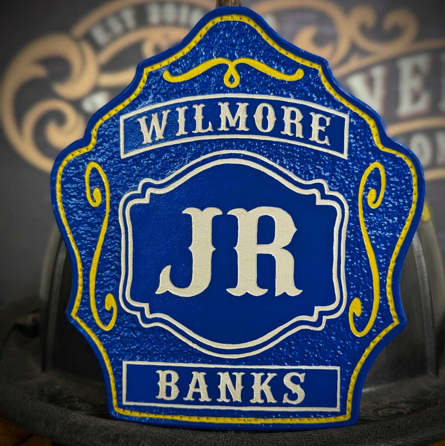 Blue leather firefighter helmet shield with bold white JR letters, Wilmore banner at the top, Banks nameplate at the bottom, and yellow decorative accents.
