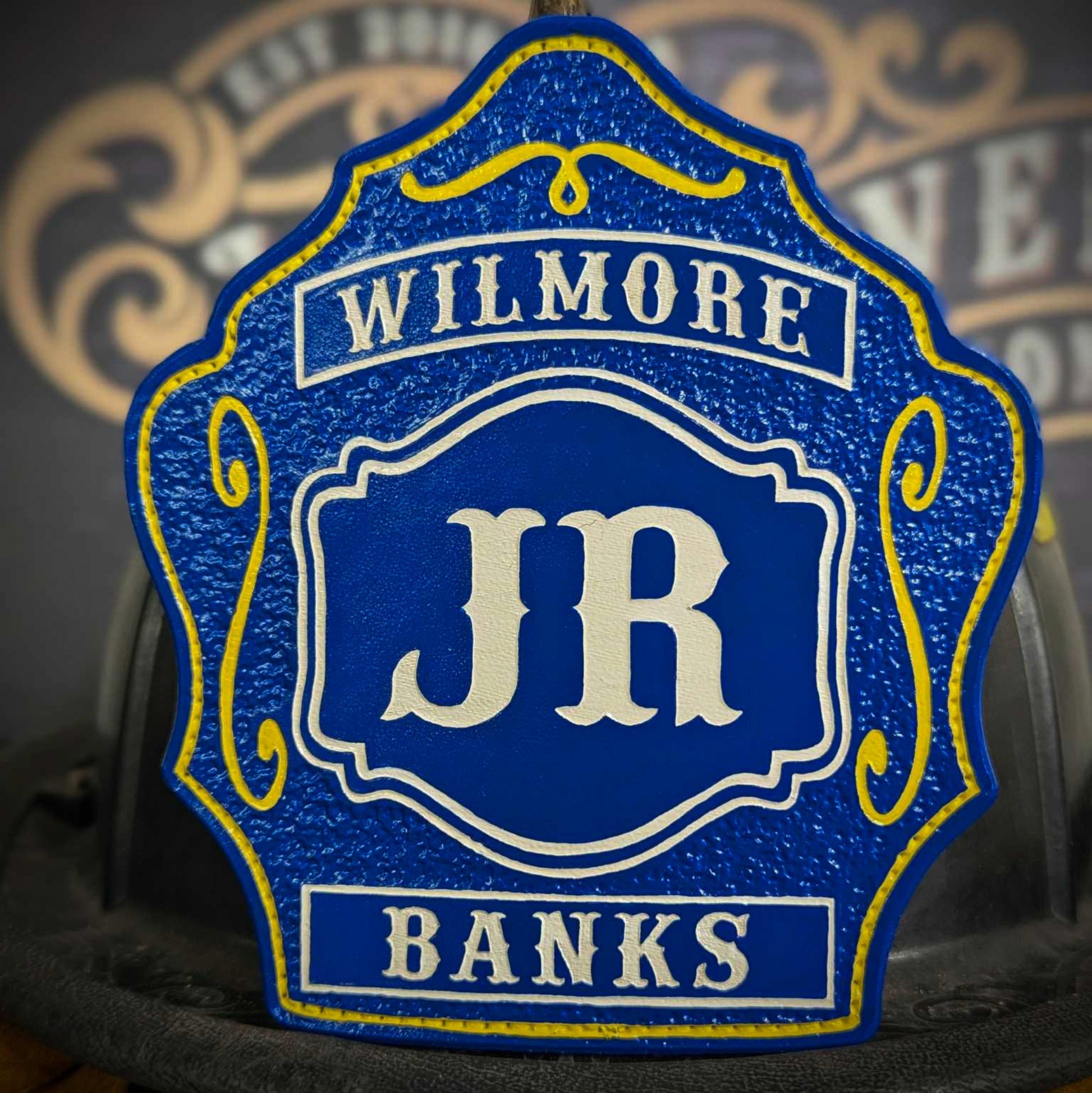 Blue leather firefighter helmet shield with bold white JR letters, Wilmore banner at the top, Banks nameplate at the bottom, and yellow decorative accents.
