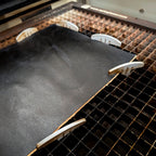 Laser bed dogs holding a leather sheet flat on a honeycomb cutting bed.