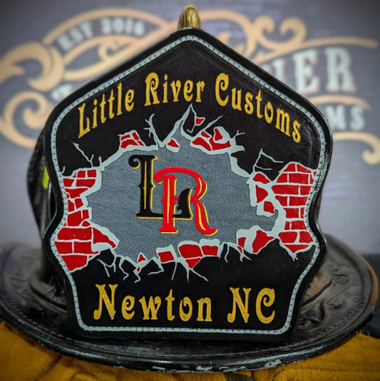 Custom leather firefighter helmet shield with cracked brick wall graphic and central monogram on a gray/black field—hand-painted and mounted on a helmet.