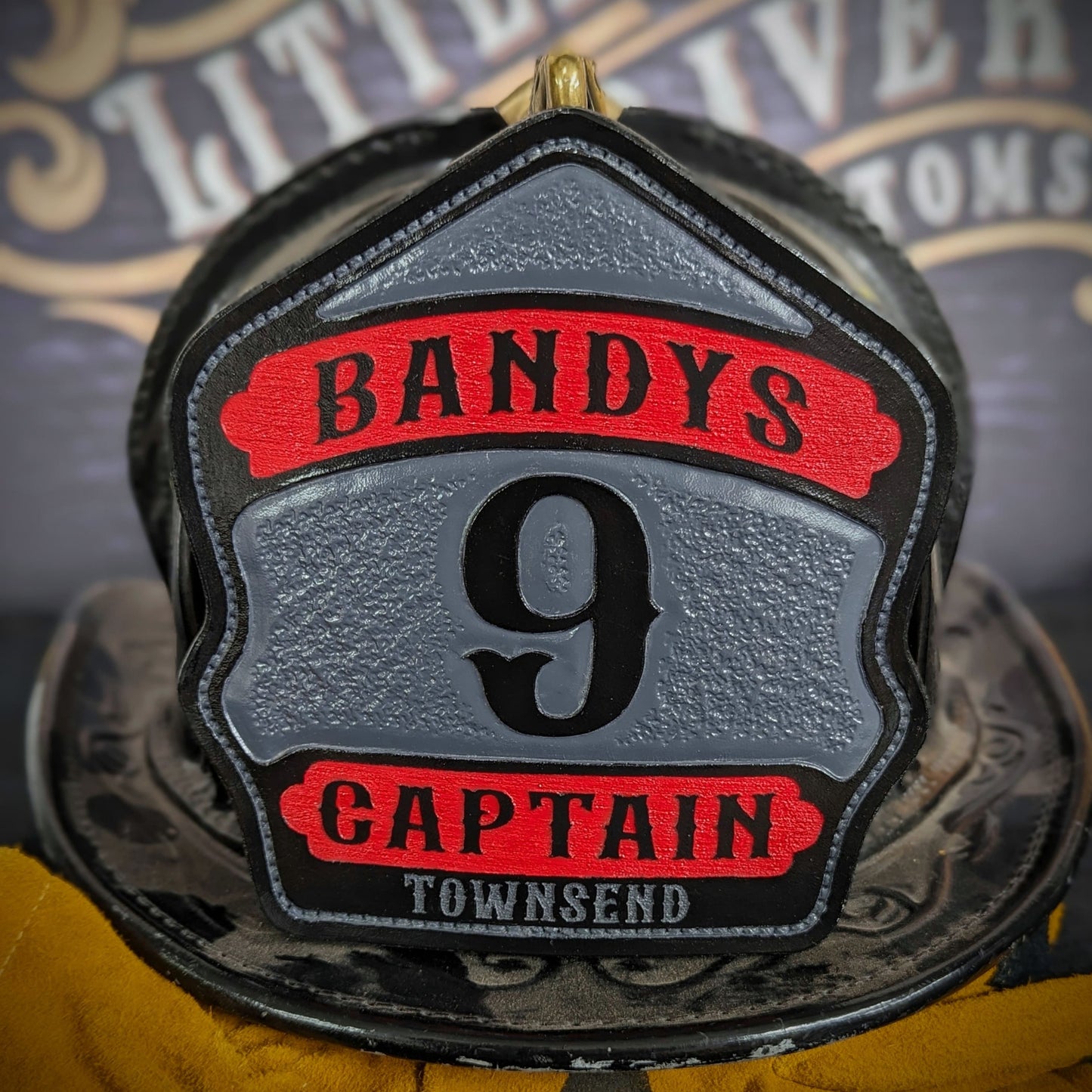 Custom leather firefighter helmet shield with gray center panel, red top and bottom banners, and black numeral—captain layout on a helmet.