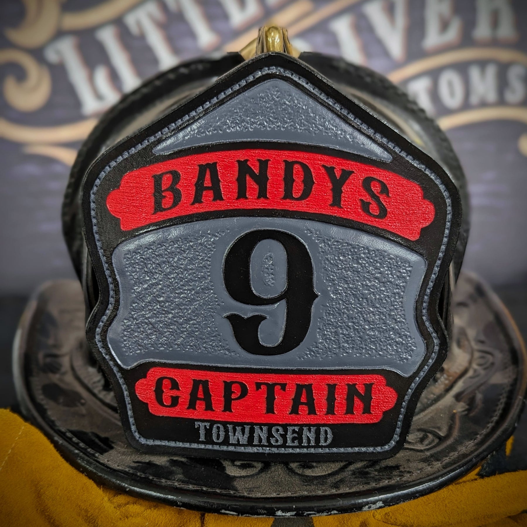 Custom leather firefighter helmet shield with gray center panel, red top and bottom banners, and black numeral—captain layout on a helmet.