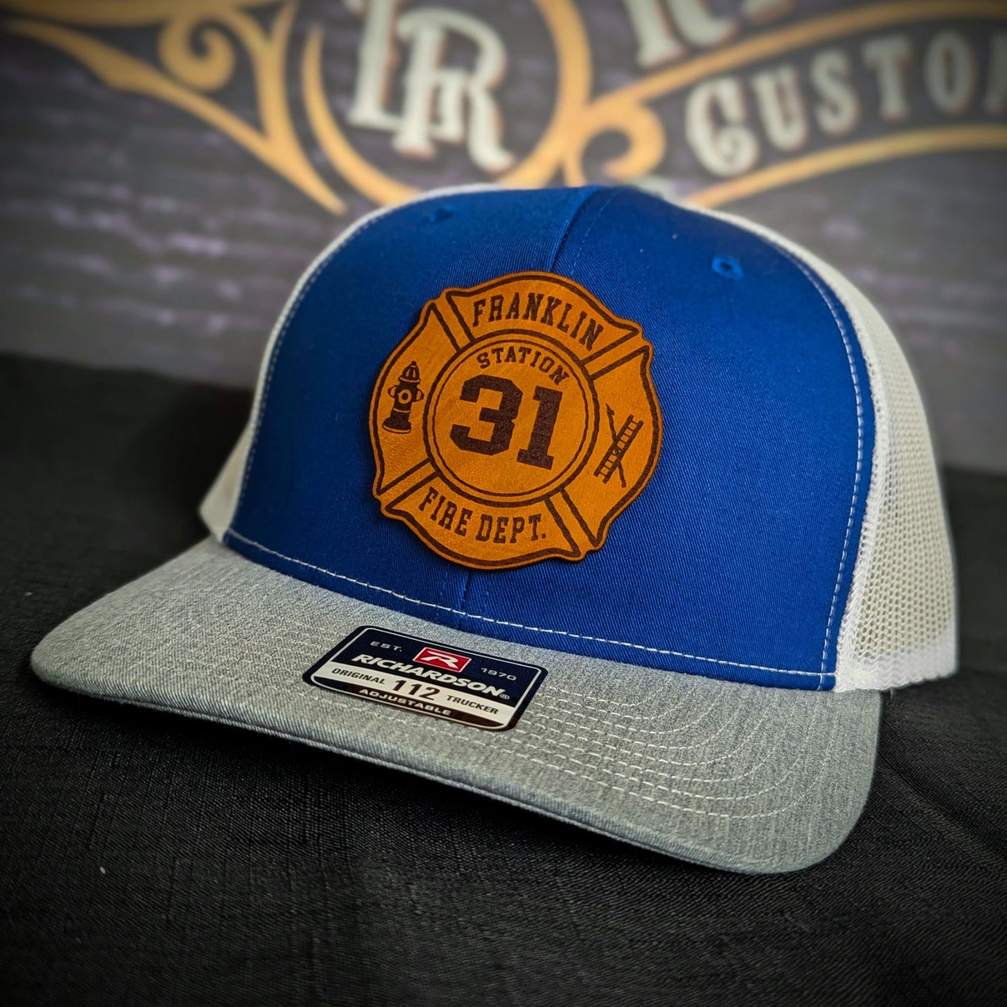 Blue and gray Richardson firefighter hat with custom Maltese leather patch design, rugged fire department headwear.