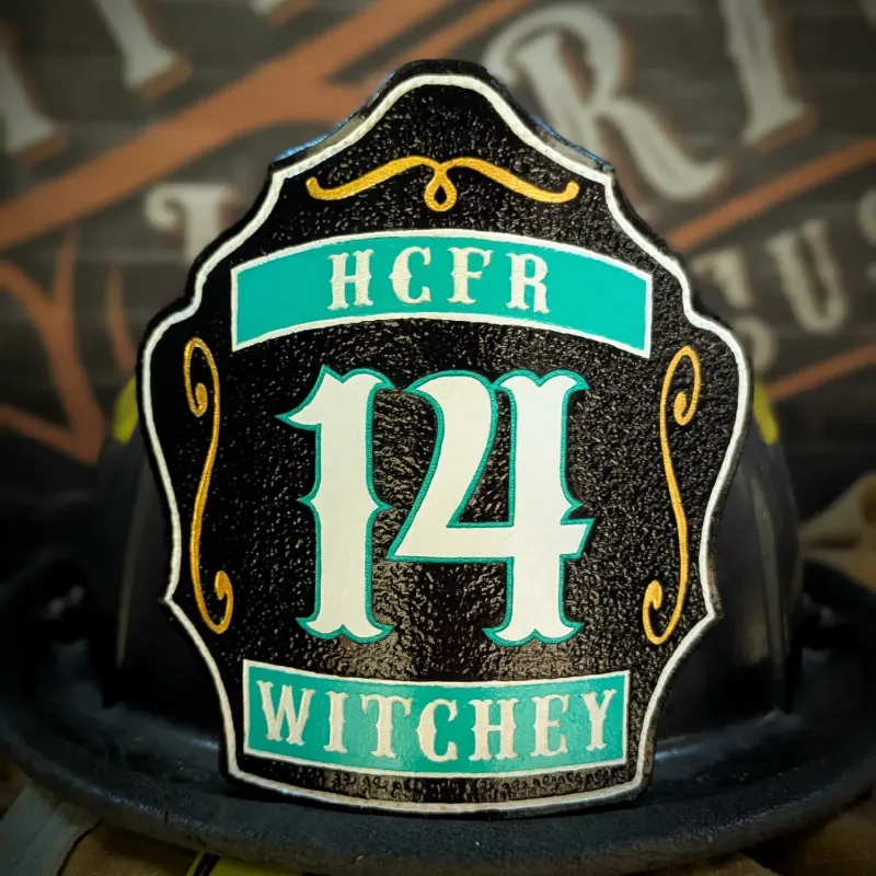 Standard Issue custom leather firefighter helmet shield in black with teal panels, white numbers, and decorative gold accents.
