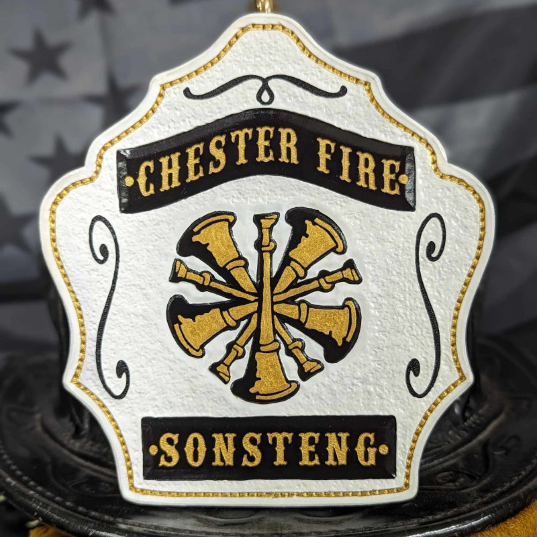 White firefighter helmet shield with gold crossed bugles and classic scroll border.