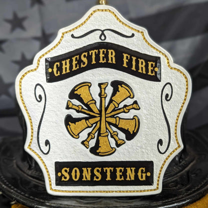 White firefighter helmet shield with gold crossed bugles and classic scroll border.