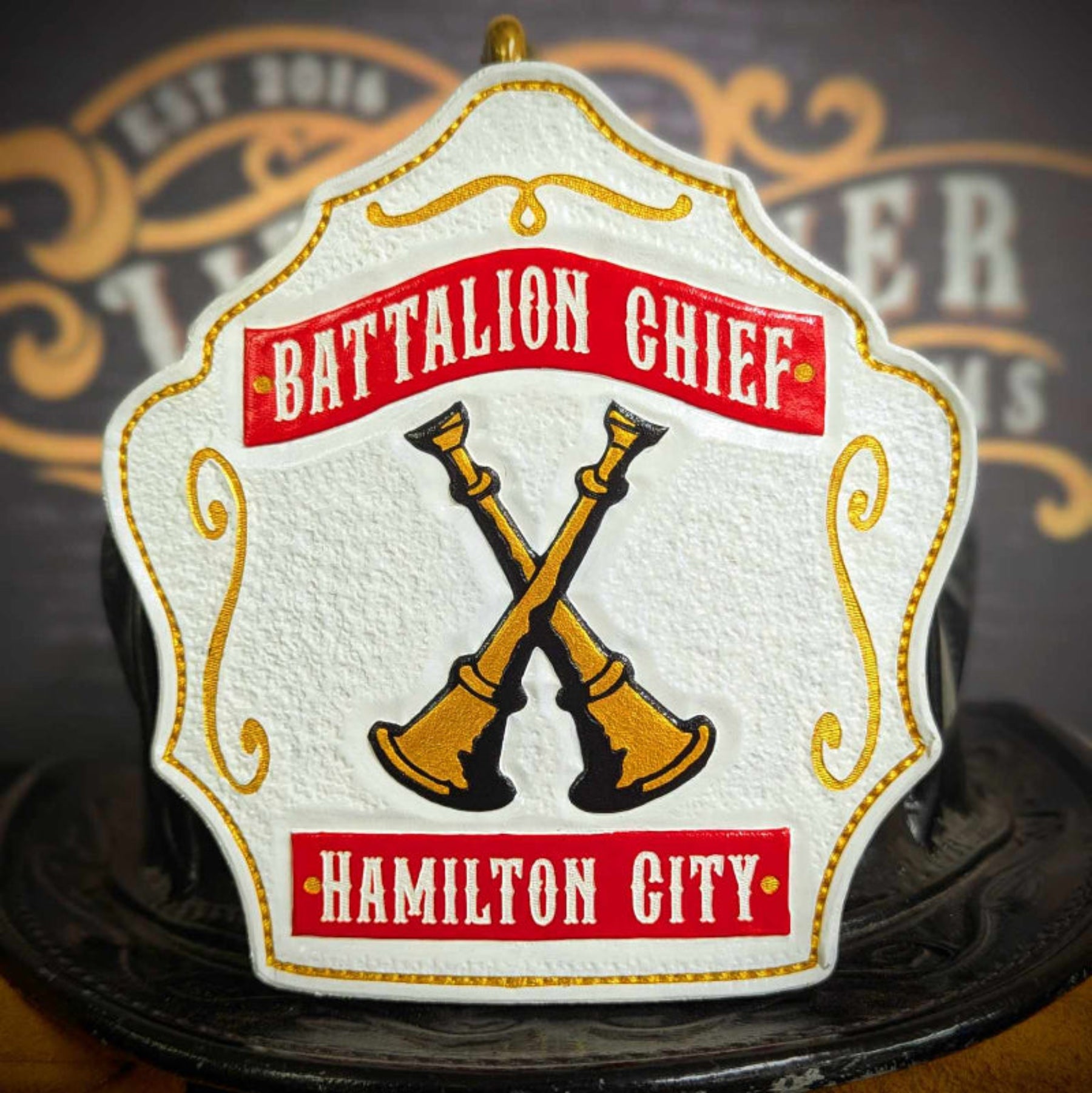 White firefighter helmet shield with red banners and gold crossed bugles on a black outline.