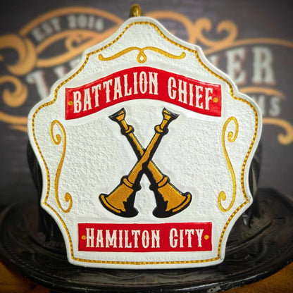White firefighter helmet shield with red banners and gold crossed bugles on a black outline.