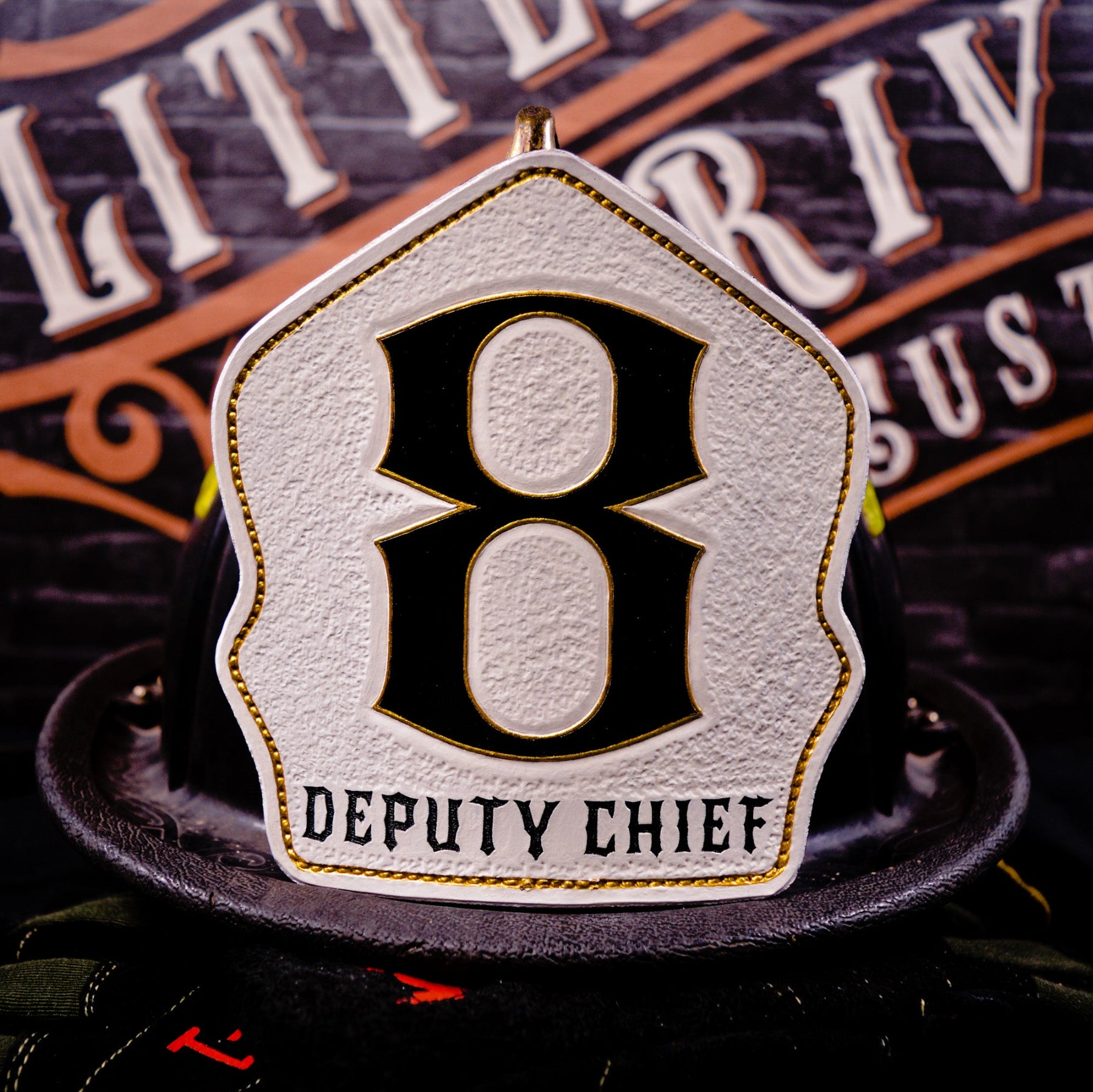 White leather firefighter helmet shield with large black “8” outlined in gold and a “DEPUTY CHIEF” title—mounted on a helmet