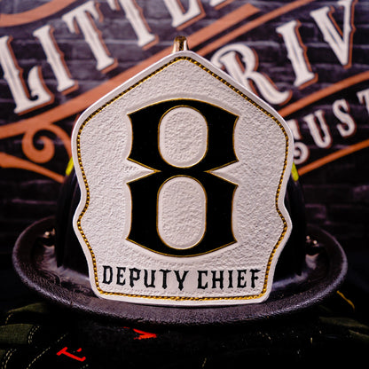 White leather firefighter helmet shield with large black “8” outlined in gold and a “DEPUTY CHIEF” title—mounted on a helmet