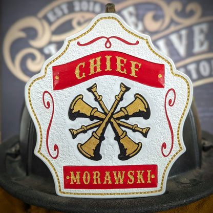 White leather firefighter helmet shield with crossed gold bugles and red banners—hand-painted and mounted on a helmet