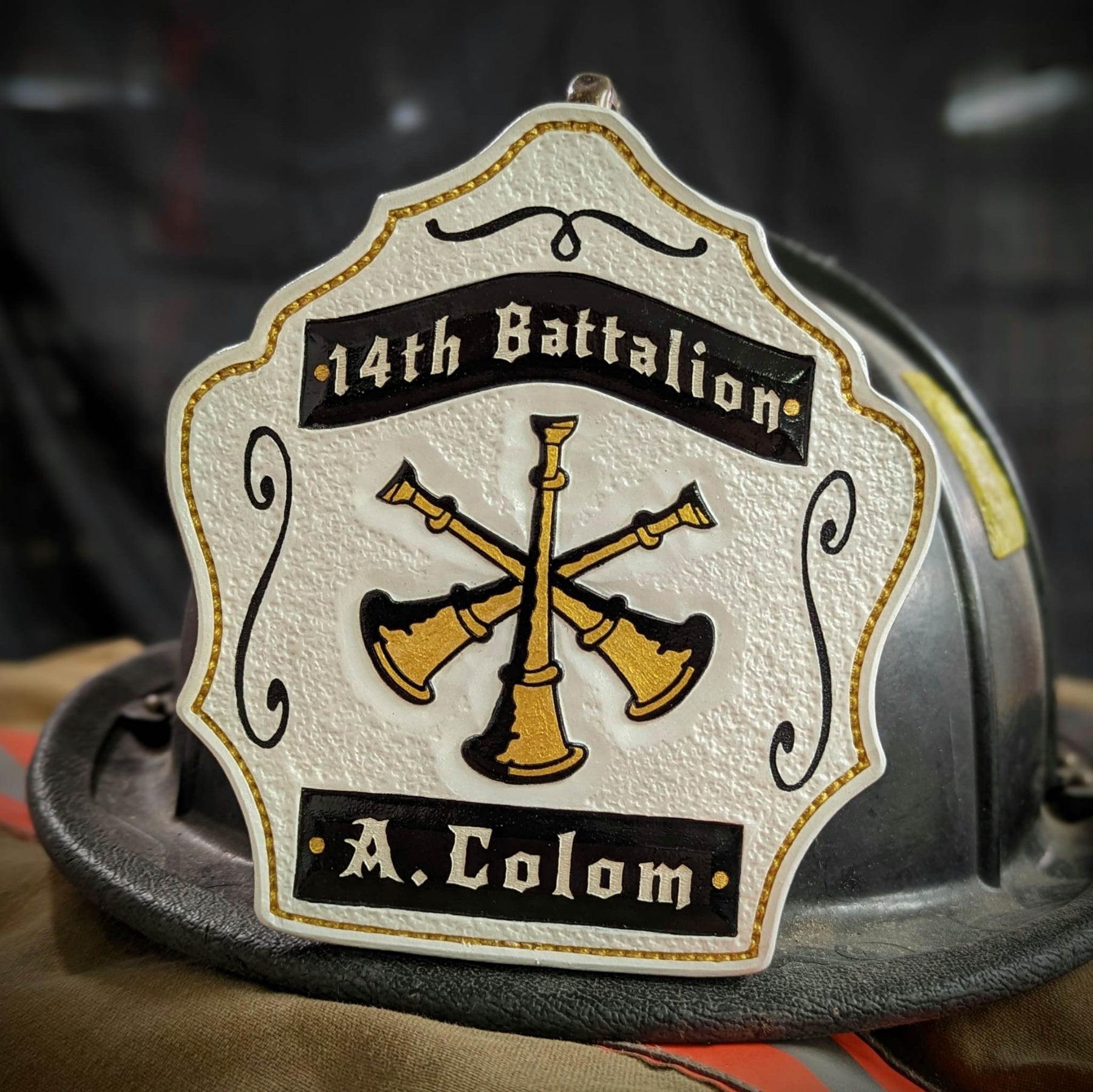 White leather firefighter helmet shield with gold crossed bugles and black banners—hand-painted and mounted on a helmet.