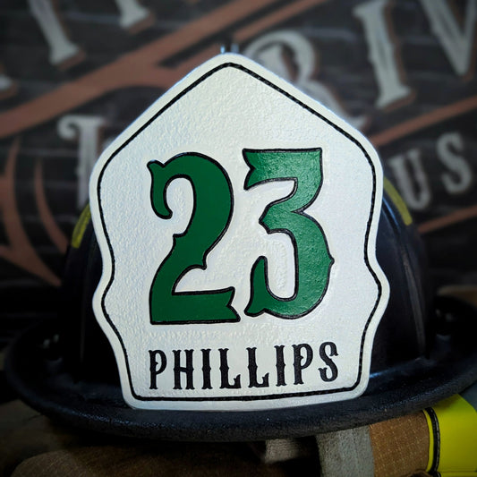 White leather firefighter helmet shield with large green numerals “23” and black name lettering—hand-painted and mounted on a helmet.