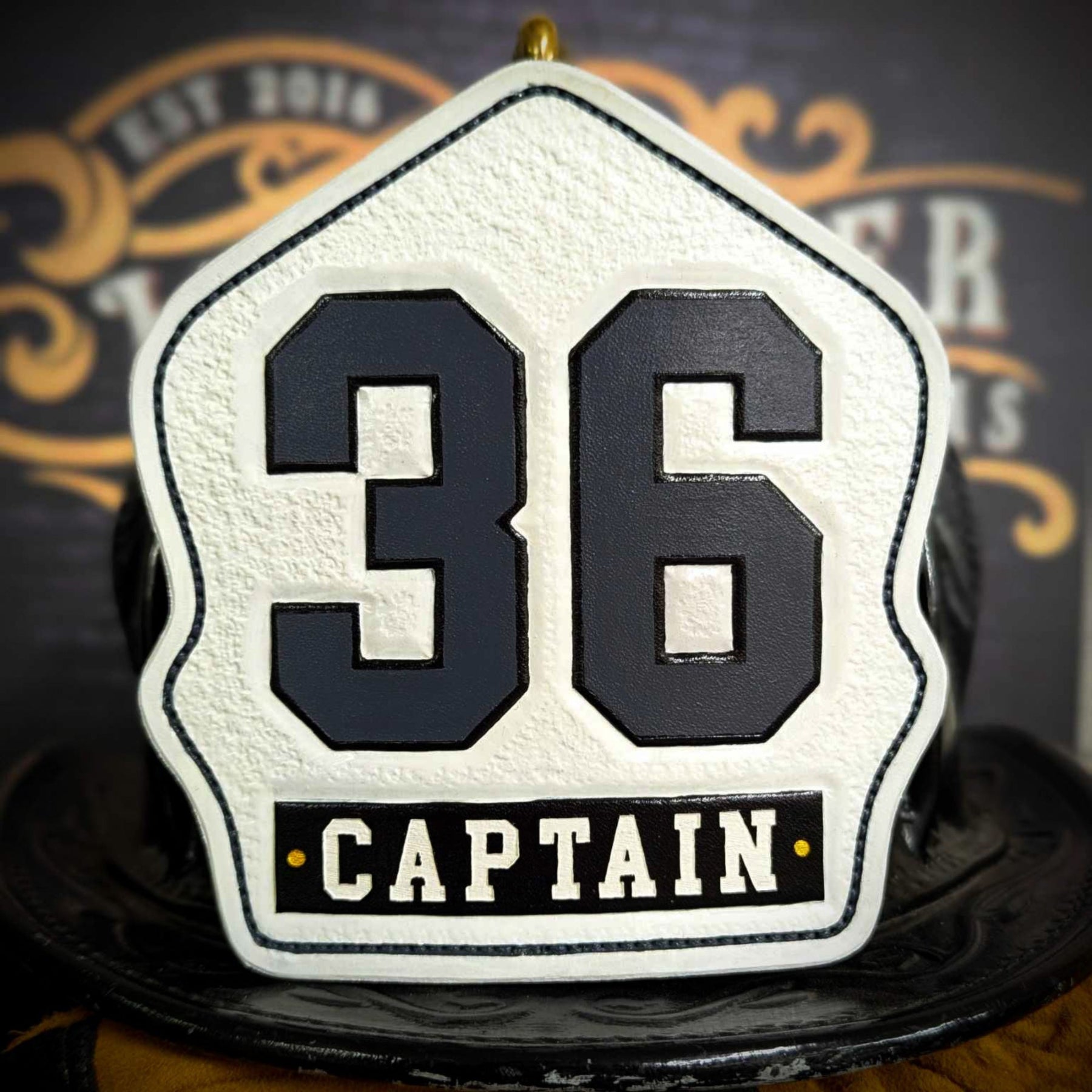 White leather firefighter helmet shield with raised gray numerals “36” and a black CAPTAIN title panel—hand-painted and mounted on a helmet.