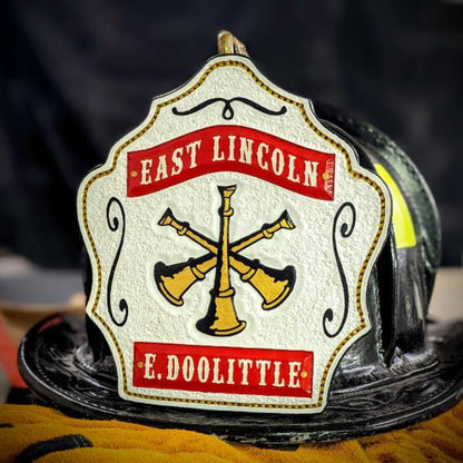 White firefighter helmet shield with gold crossed bugles and “chief of department” layout
